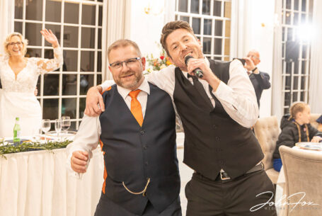 A singing waiter with Kevin the groom at his Rushton Hall Wedding with his bride, Joanne, dancing in the background.
