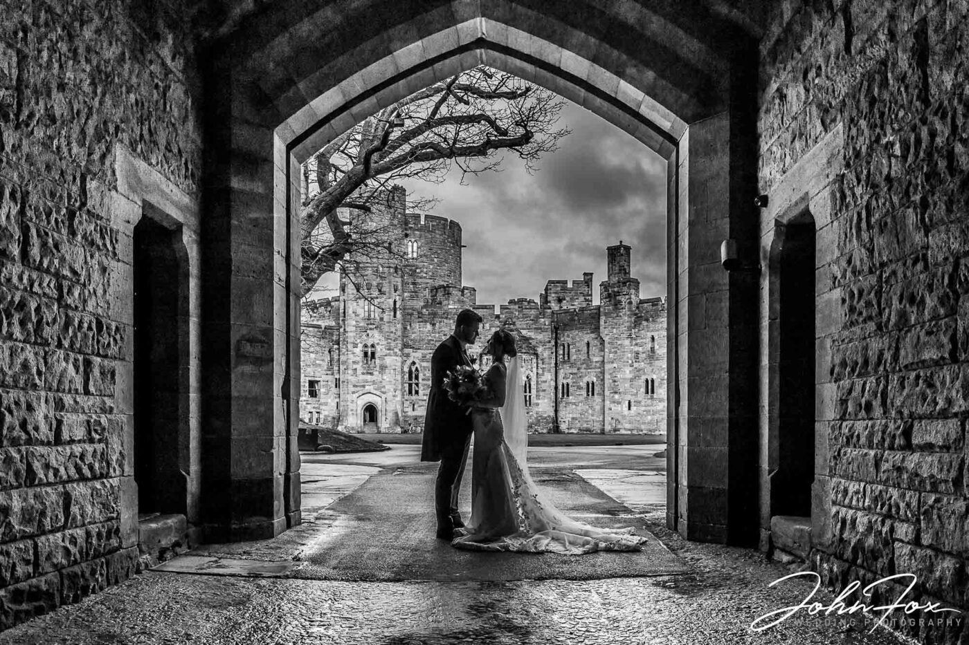 Jenny and James’s day at Peckforton Castle. The couple in an archway in the grounds of the historic wedding venue. Cheshire wedding photographer packages from John Fox.