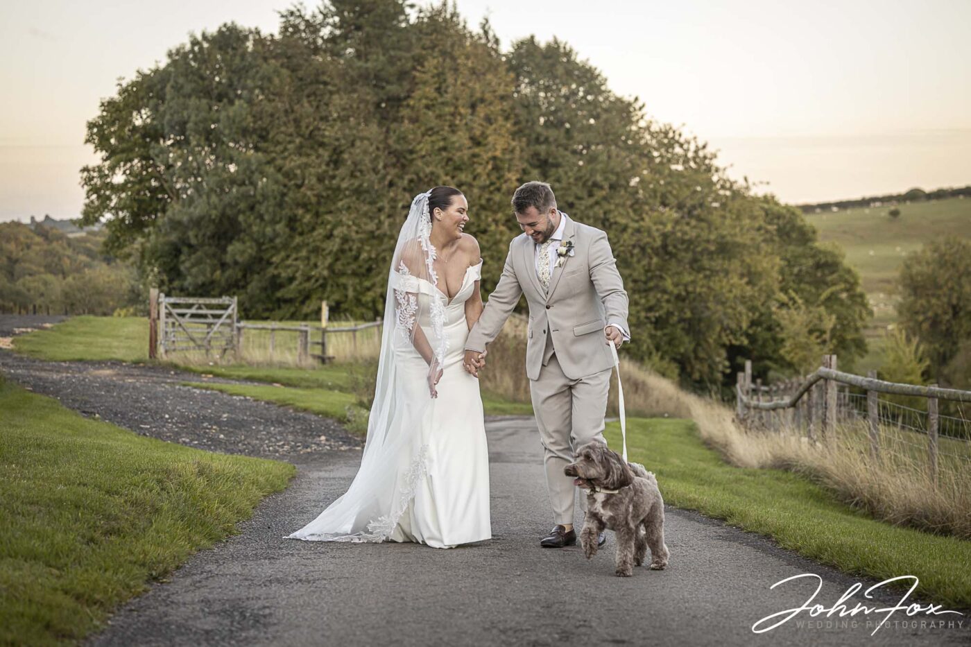 Gabrielle and William and their dog exploring the grounds at Kingscote Barn in the Cotswolds, Gloucestershire on their wedding day.