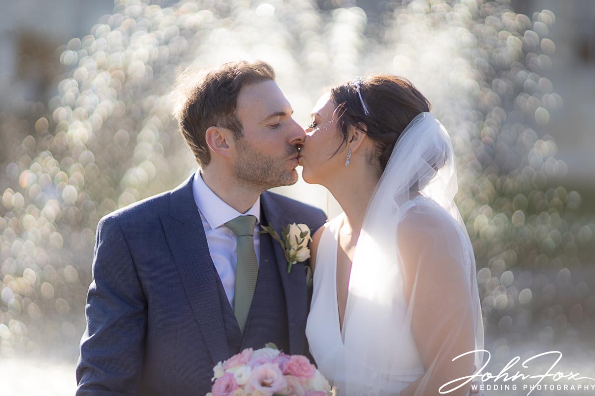 Nicole and Nicholas kissing by a fountain at Ashridge House. John Fox Wedding Photography in Hertfordshire