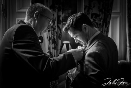 Groomsmen helping each other in preparation for Eleanor and Oliver's wedding at Kilworth House in Leicester