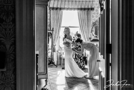 Eleanor, the bride, being helped with her dress. Wedding Photographer at Kilworth House in Leicester