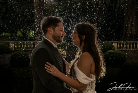 An evening image of Eleanor and Oliver holding each other in the rain. Wedding Photographer at Kilworth House in Leicester, John Fox.
