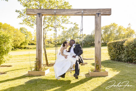 Figan and Philip kissing on a wooden-framed swing at their Milton Keynes' wedding