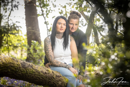 Jody and Beth holding each other while sitting on a fallen tree. Wedding Photographer in Rugby, Warwickshire - John Fox.