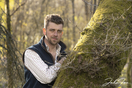 Pre-wedding shoot in Leicestershire woodland of the groom to be, Reece leaning on a moss covered tree trunk. Wedding Photographer covering Leicestershire, John Fox