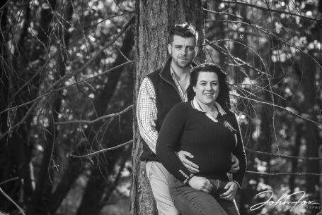Pre-wedding black and white image in Leicestershire woodland of the bride and groom to be, Paige and Reece, leaning on a tree. Wedding Photographer covering Leicestershire, John Fox.
