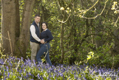 Pre-wedding image in Leicestershire woodland of the bride and groom to be, Paige and Reece, leaning on a tree amongst the bluebells. Wedding Photographer covering Leicestershire, John Fox.