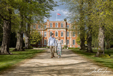 Pre-wedding shoot at Chicheley Hall of the couple, Jayne and Craig, walking on the driveway with venue behind. Wedding Photographer in Buckinghamshire, John Fox.