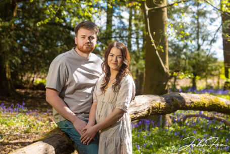 An image of Rikki leaning on Jack as he sits on a fallen tree. Pre-wedding shoot in Warwickshire woodland. Wedding Photographer in the West Midlands, John Fox.