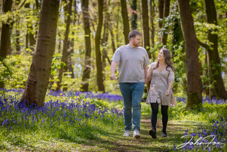 An image of the happy couple, Rikki and Jack, chatting while walking amongst the trees and bluebells. Pre-wedding shoot in Warwickshire woodland. Wedding Photographer in the West Midlands, John Fox.