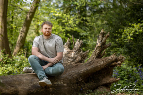 Pre-wedding shoot in Warwickshire woodland. An image of the groom-to-be, Jack, sitting on a fallen tree. Wedding Photographer in the West Midlands, John Fox.