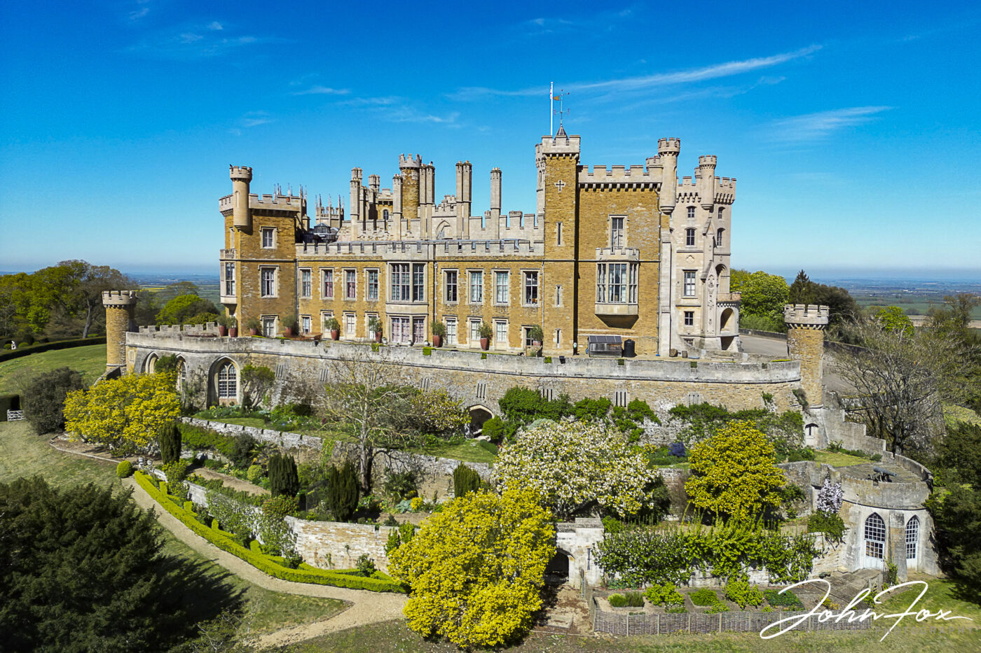 Stunning aerial view of Belvoir Castle with a bright blue sky framing it.